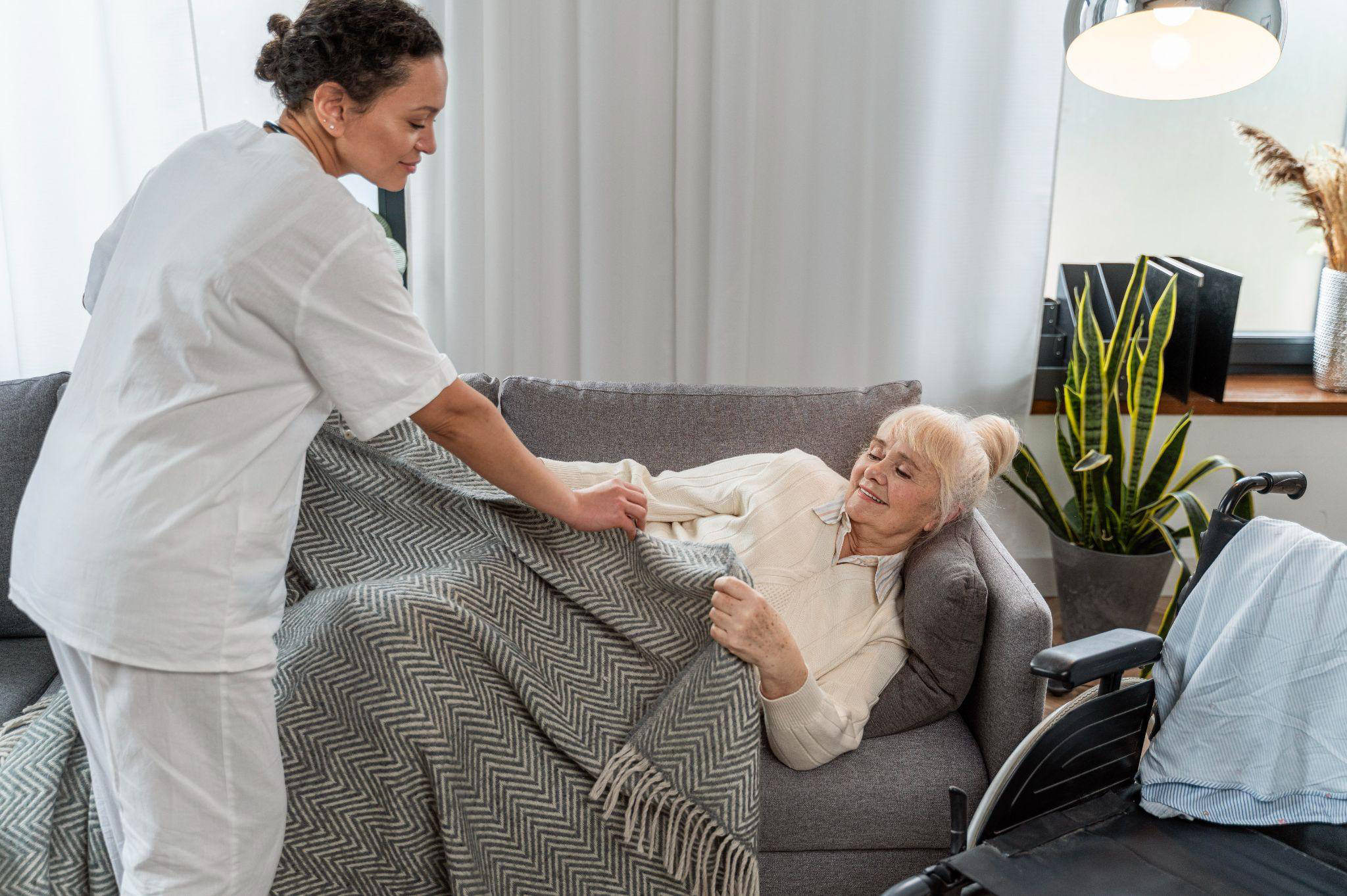 A caregiver providing consistent home health care support to a senior woman resting on a couch at home